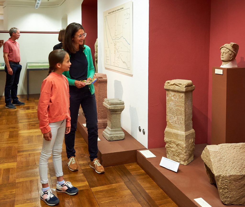 Eine Frau und ein Mädchen betrachten historische Steindenkmäler und Ausstellungsstücke im Städtischen Museum Bruchsal.